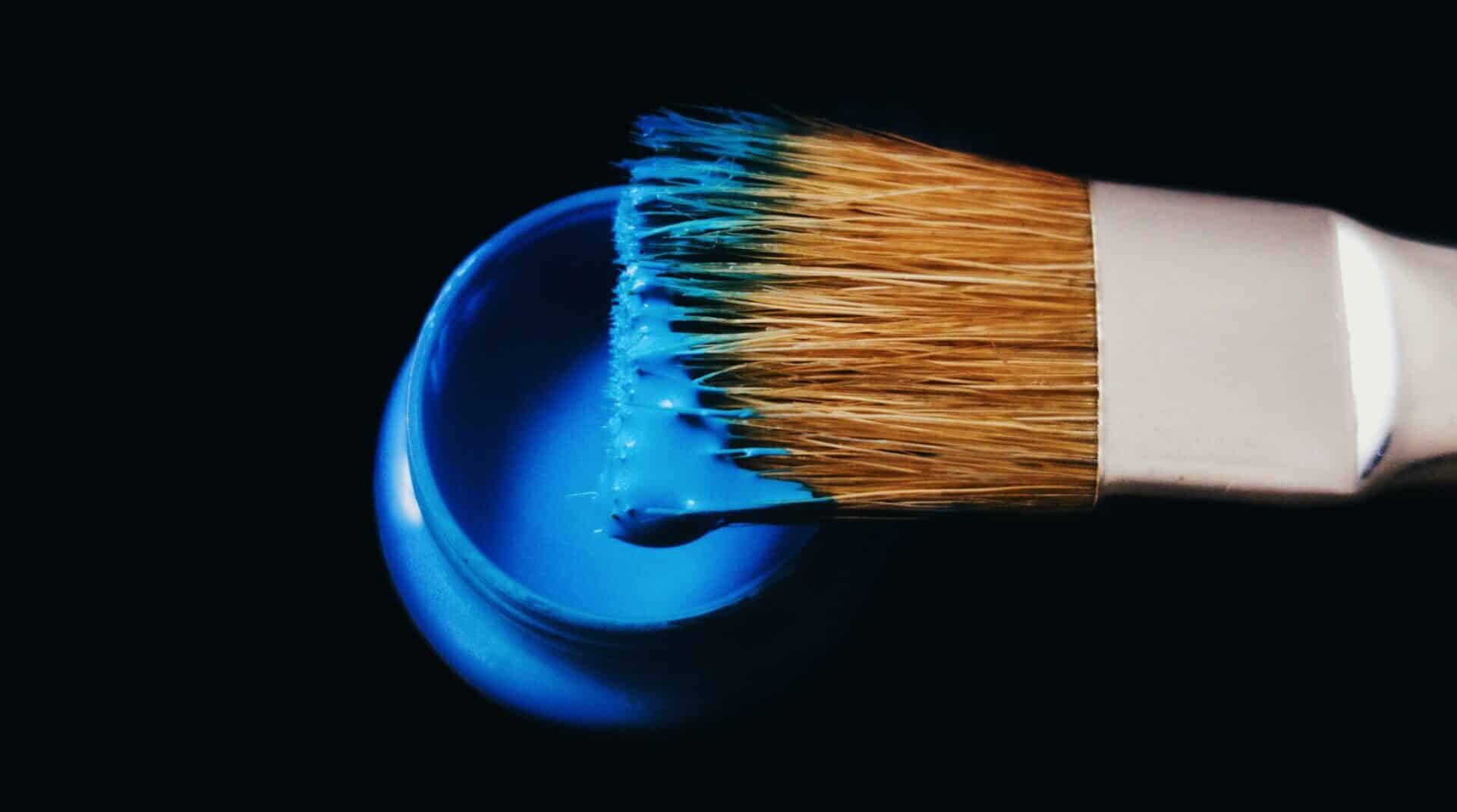 close up of a paint brush over a bucket of bright blue paint